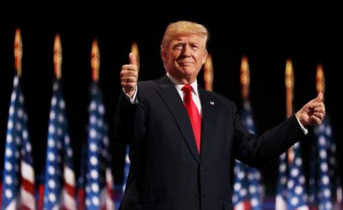 President-Trump standing thumbs up in front of flags